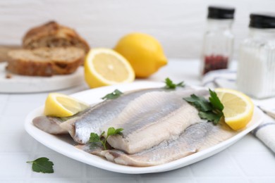 Photo of Marinated herring fillets with lemon and parsley on white tiled table, closeup