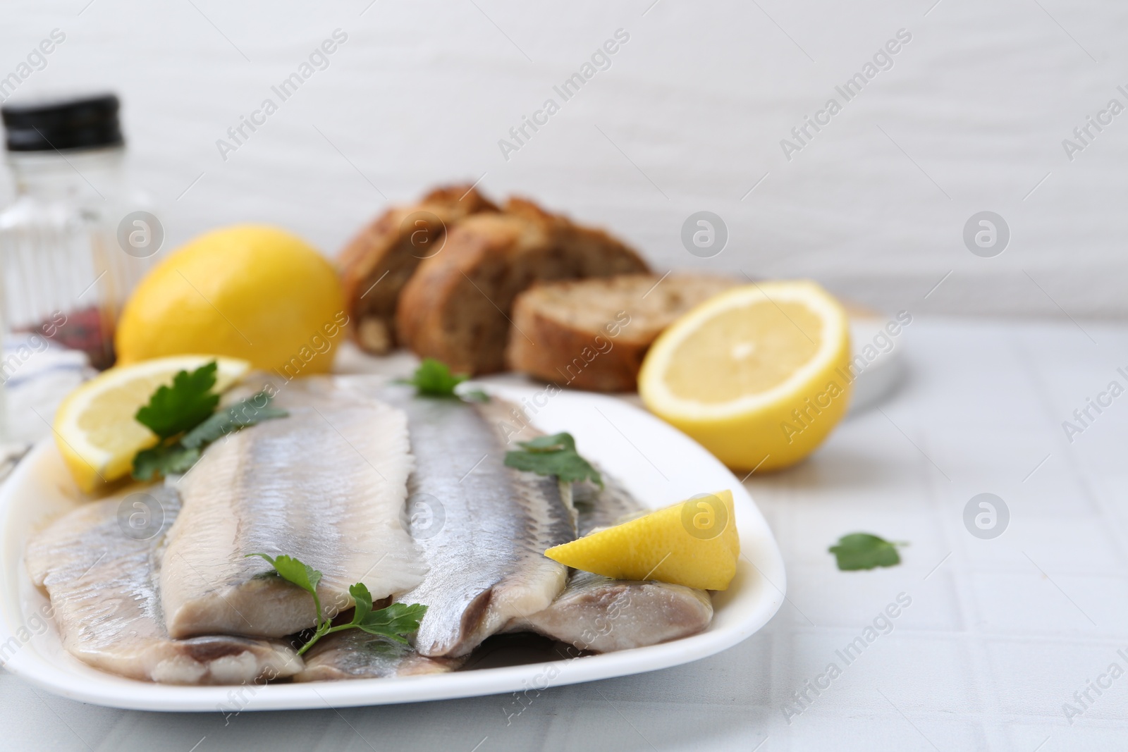 Photo of Marinated herring fillets with lemon and parsley on white tiled table, closeup. Space for text