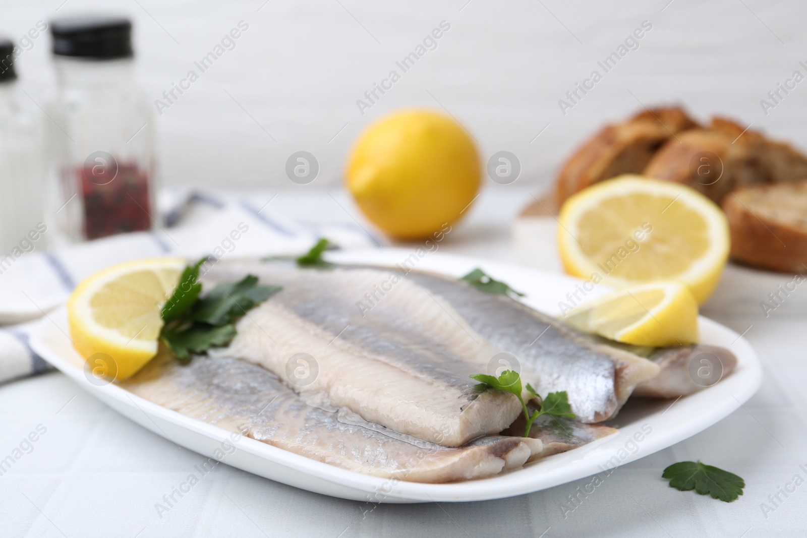 Photo of Marinated herring fillets with lemon and parsley on white tiled table, closeup