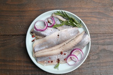 Marinated herring fillets with onion rings, rosemary and peppercorns on wooden table, top view