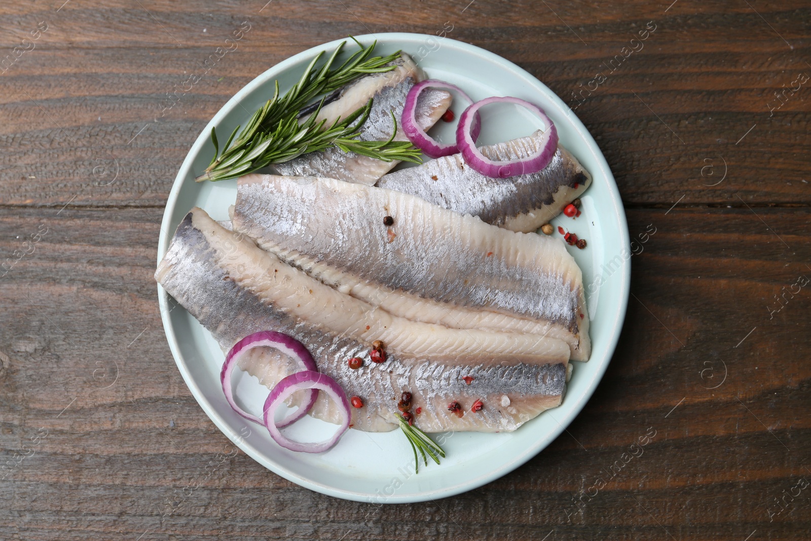 Photo of Marinated herring fillets with onion rings, rosemary and peppercorns on wooden table, top view