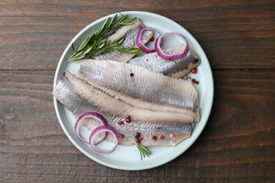 Photo of Marinated herring fillets with onion rings, rosemary and peppercorns on wooden table, top view