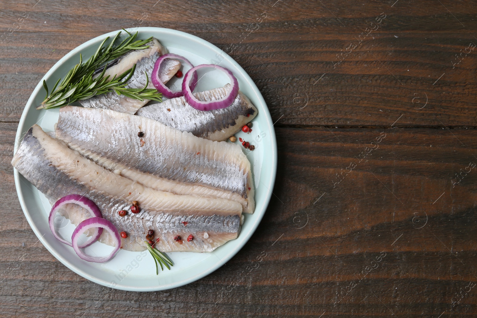 Photo of Marinated herring fillets with onion rings, rosemary and peppercorns on wooden table, top view. Space for text