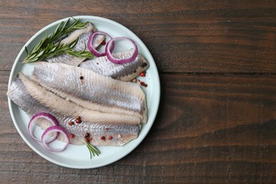 Marinated herring fillets with onion rings, rosemary and peppercorns on wooden table, top view. Space for text