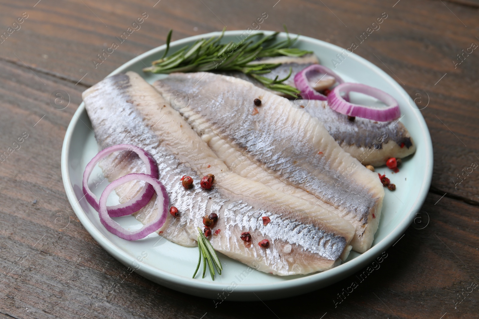 Photo of Marinated herring fillets with onion rings, rosemary and peppercorns on wooden table, closeup