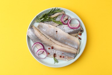 Photo of Marinated herring fillets with onion rings, rosemary and peppercorns on yellow background, top view