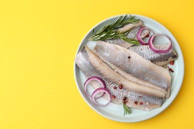 Photo of Marinated herring fillets with onion rings, rosemary and peppercorns on yellow background, top view. Space for text