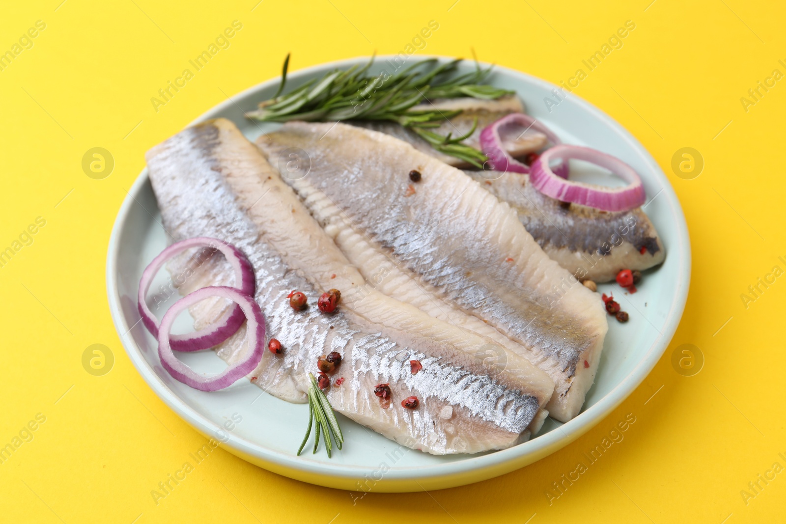 Photo of Marinated herring fillets with onion rings, rosemary and peppercorns on yellow background, closeup