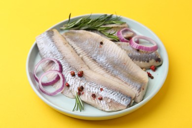 Photo of Marinated herring fillets with onion rings, rosemary and peppercorns on yellow background, closeup