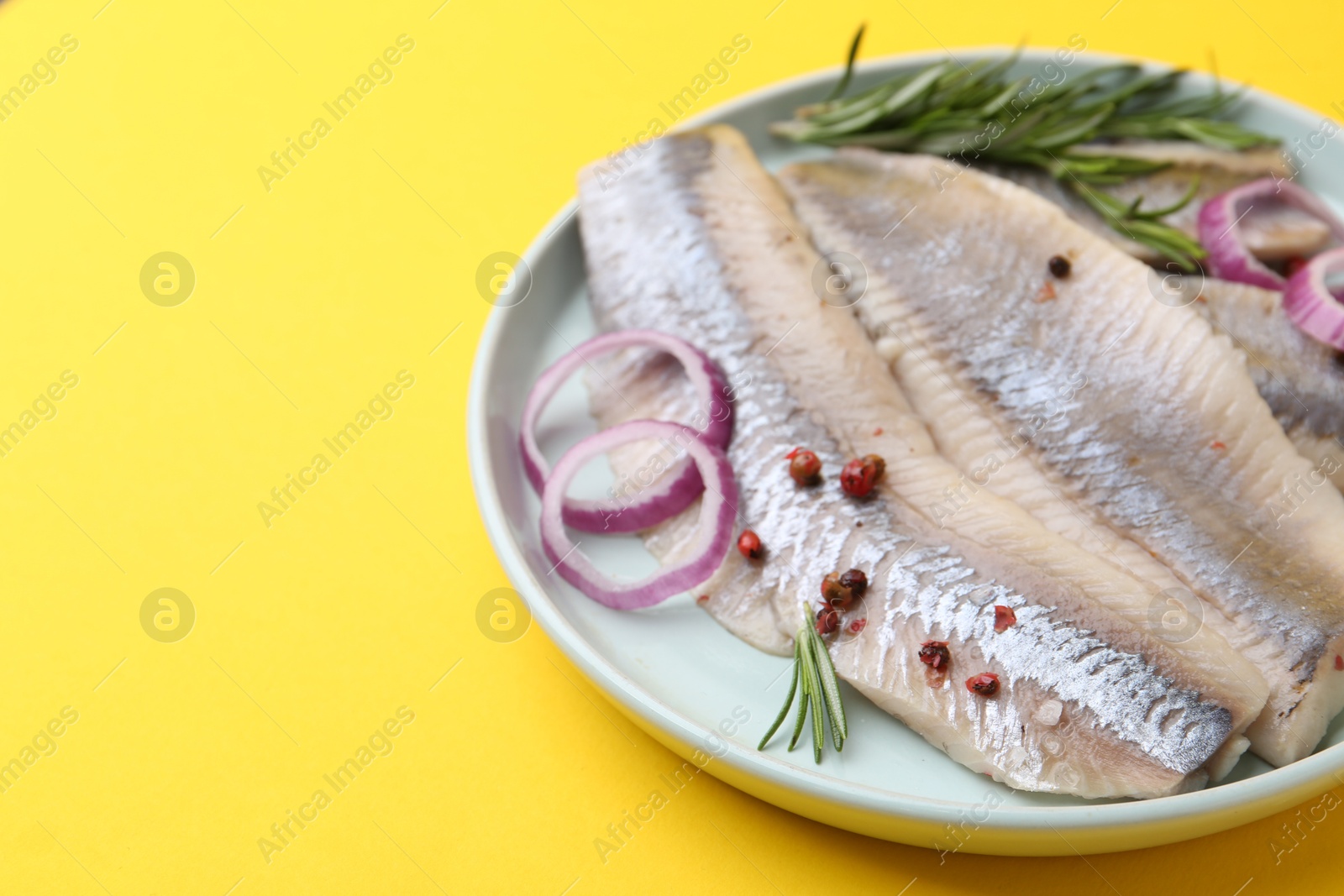 Photo of Marinated herring fillets with onion rings, rosemary and peppercorns on yellow background, closeup. Space for text