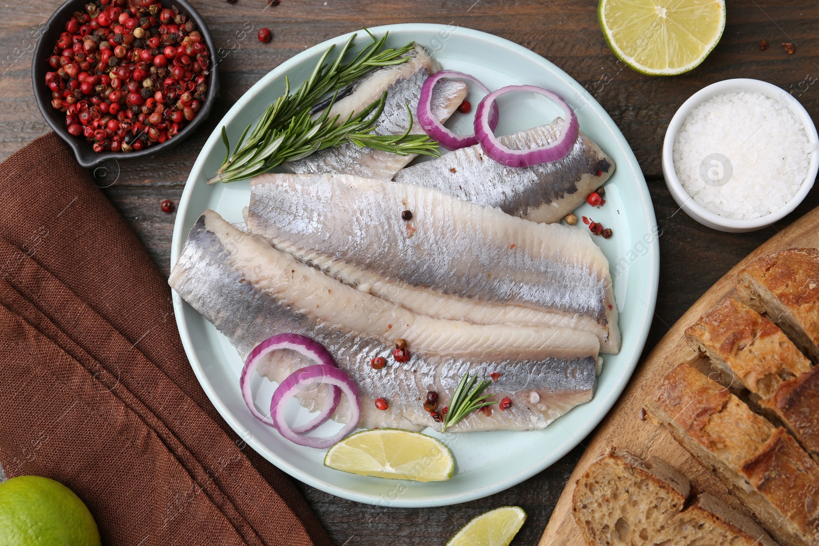 Photo of Marinated herring fillets with onion rings, rosemary, lime and spices on wooden table, flat lay