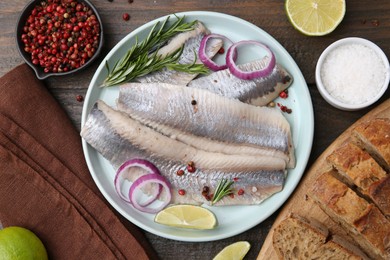 Marinated herring fillets with onion rings, rosemary, lime and spices on wooden table, flat lay