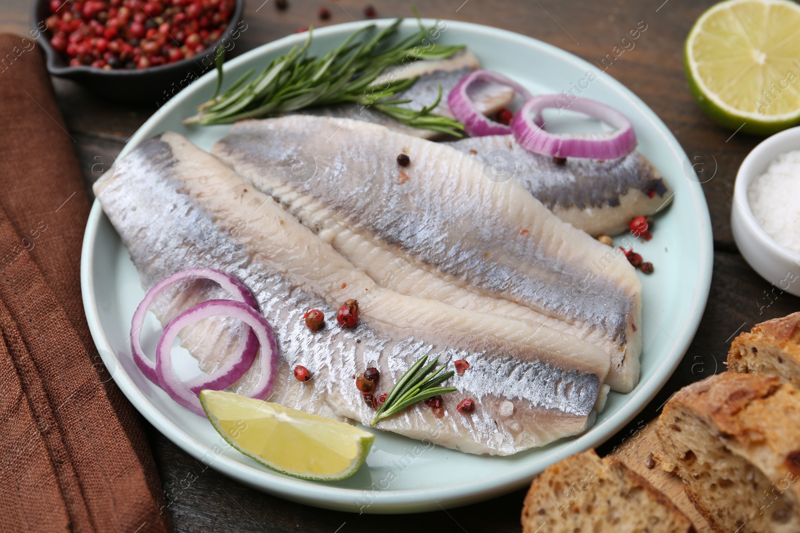 Photo of Marinated herring fillets with onion rings, rosemary, lime and spices on wooden table, closeup