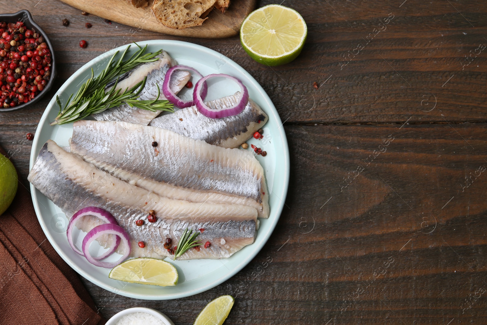 Photo of Marinated herring fillets with onion rings, rosemary, lime and spices on wooden table, flat lay. Space for text