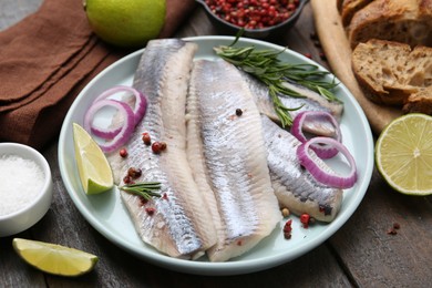 Photo of Marinated herring fillets with onion rings, rosemary, lime and spices on wooden table, closeup