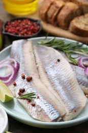 Photo of Marinated herring fillets with onion rings, rosemary, lime and peppercorns on table, closeup