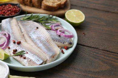 Photo of Marinated herring fillets with onion rings, rosemary, lime and peppercorns on wooden table, closeup. Space for text