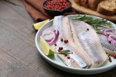 Photo of Marinated herring fillets with onion rings, rosemary, lime and peppercorns on wooden table, closeup. Space for text