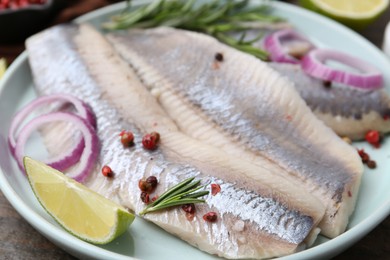 Photo of Marinated herring fillets with onion rings, rosemary, lime and peppercorns on table, closeup