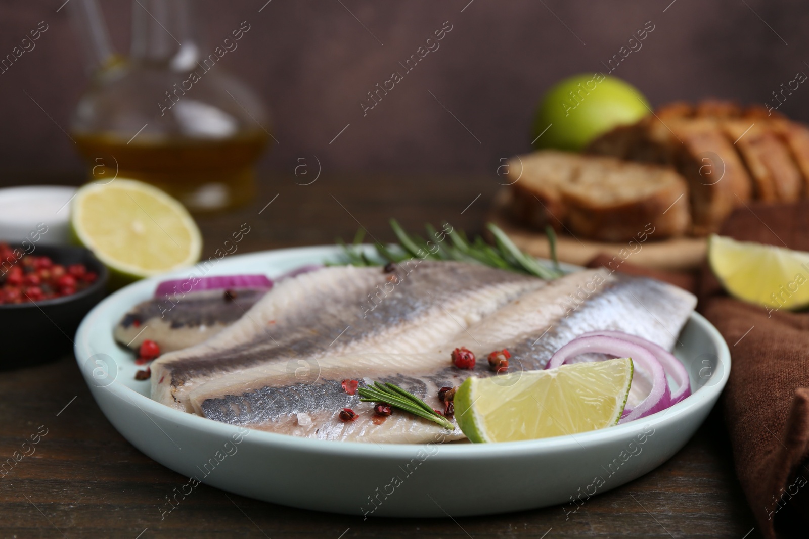 Photo of Marinated herring fillets with onion rings, rosemary, lime and peppercorns on wooden table, closeup