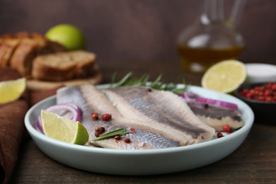 Marinated herring fillets with onion rings, rosemary, lime and peppercorns on wooden table, closeup