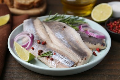 Photo of Marinated herring fillets with onion rings, rosemary, lime and peppercorns on wooden table, closeup