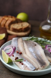 Photo of Marinated herring fillets with onion rings, rosemary, lime and peppercorns on wooden table, closeup