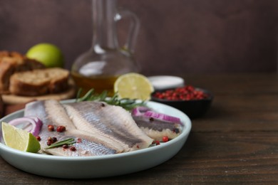 Photo of Marinated herring fillets with onion rings, rosemary, lime and peppercorns on wooden table, closeup. Space for text