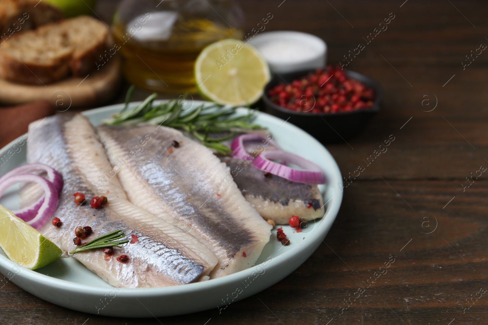 Photo of Marinated herring fillets with onion rings, rosemary, lime and peppercorns on wooden table, closeup. Space for text