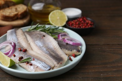 Marinated herring fillets with onion rings, rosemary, lime and peppercorns on wooden table, closeup. Space for text