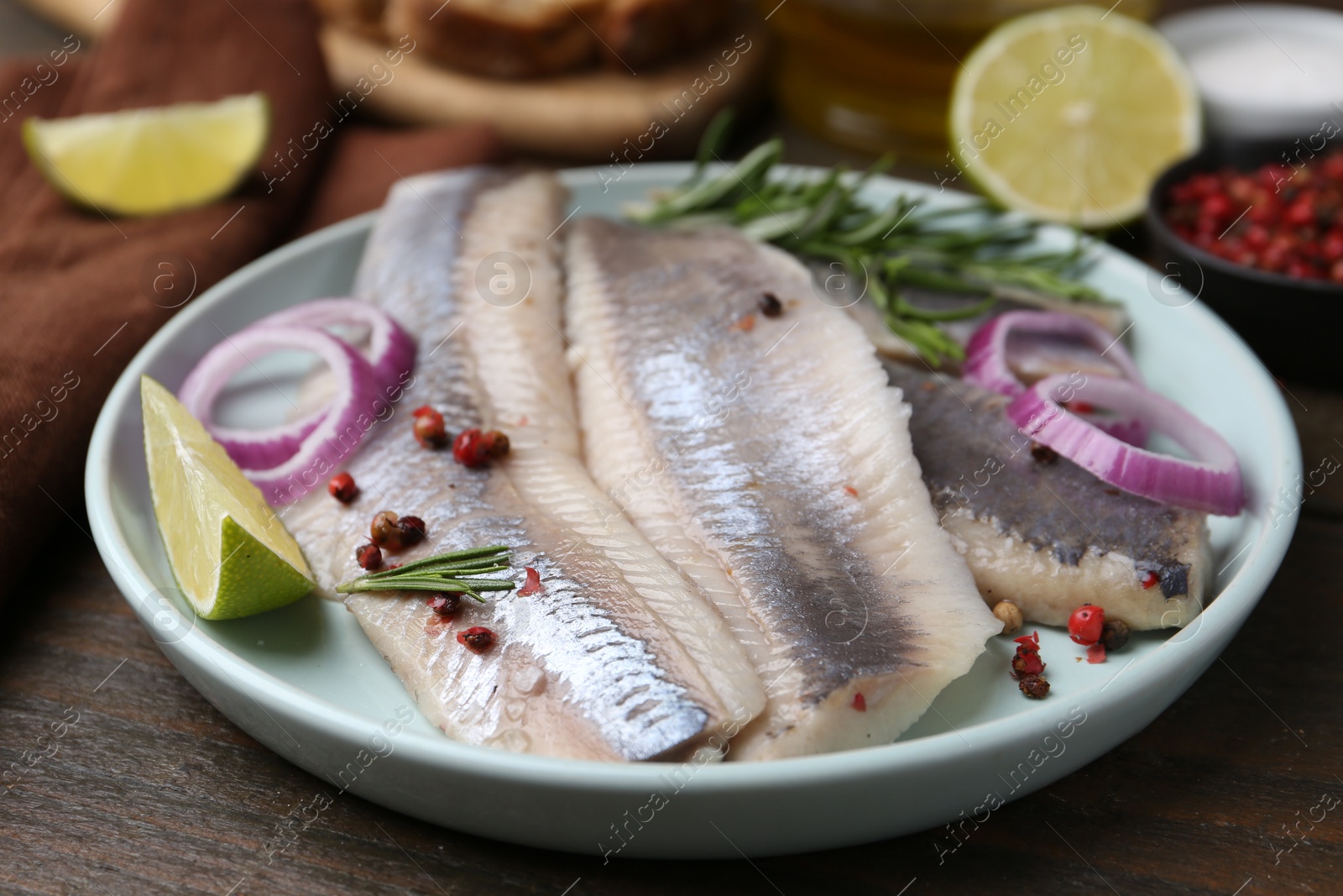 Photo of Marinated herring fillets with onion rings, rosemary, lime and peppercorns on wooden table, closeup