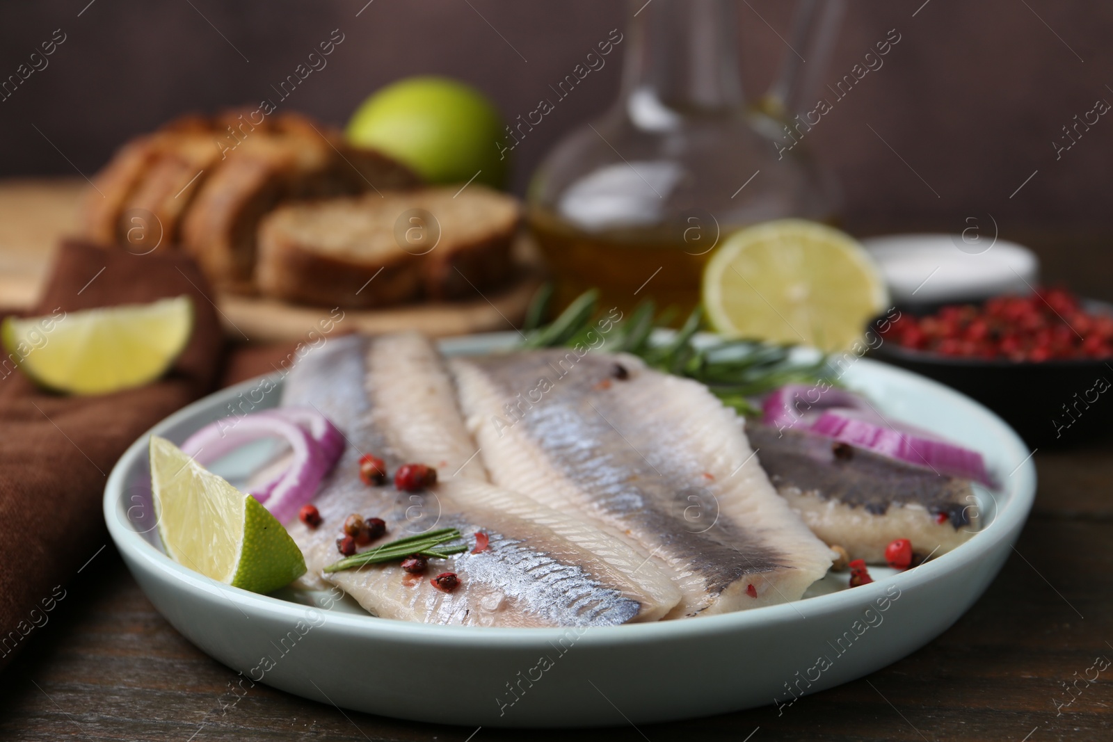 Photo of Marinated herring fillets with onion rings, rosemary, lime and peppercorns on wooden table, closeup