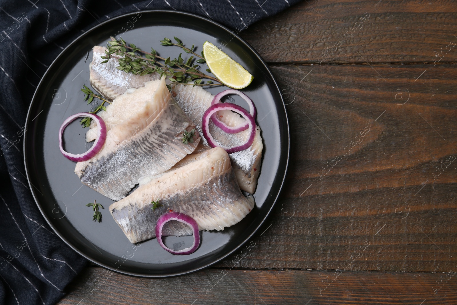 Photo of Marinated herring fillets with onion rings, thyme and lime on wooden table, top view. Space for text