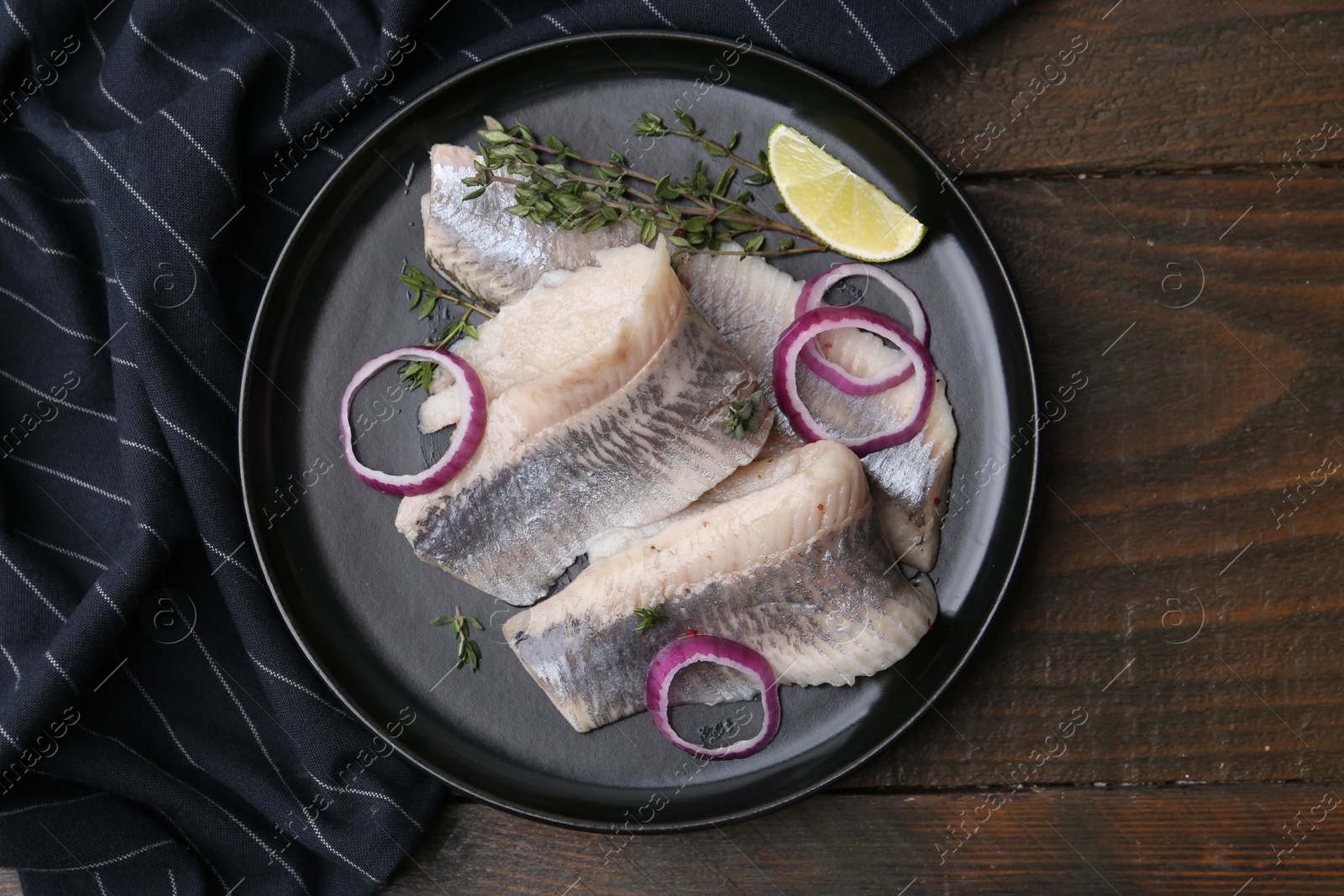 Photo of Marinated herring fillets with onion rings, thyme and lime on wooden table, top view