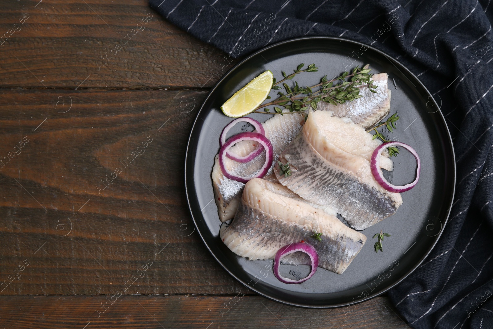 Photo of Marinated herring fillets with onion rings, thyme and lime on wooden table, top view. Space for text