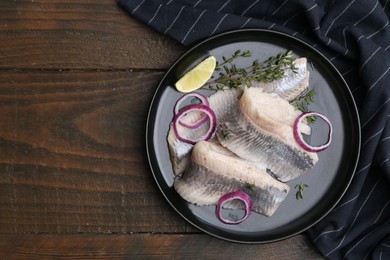 Marinated herring fillets with onion rings, thyme and lime on wooden table, top view. Space for text