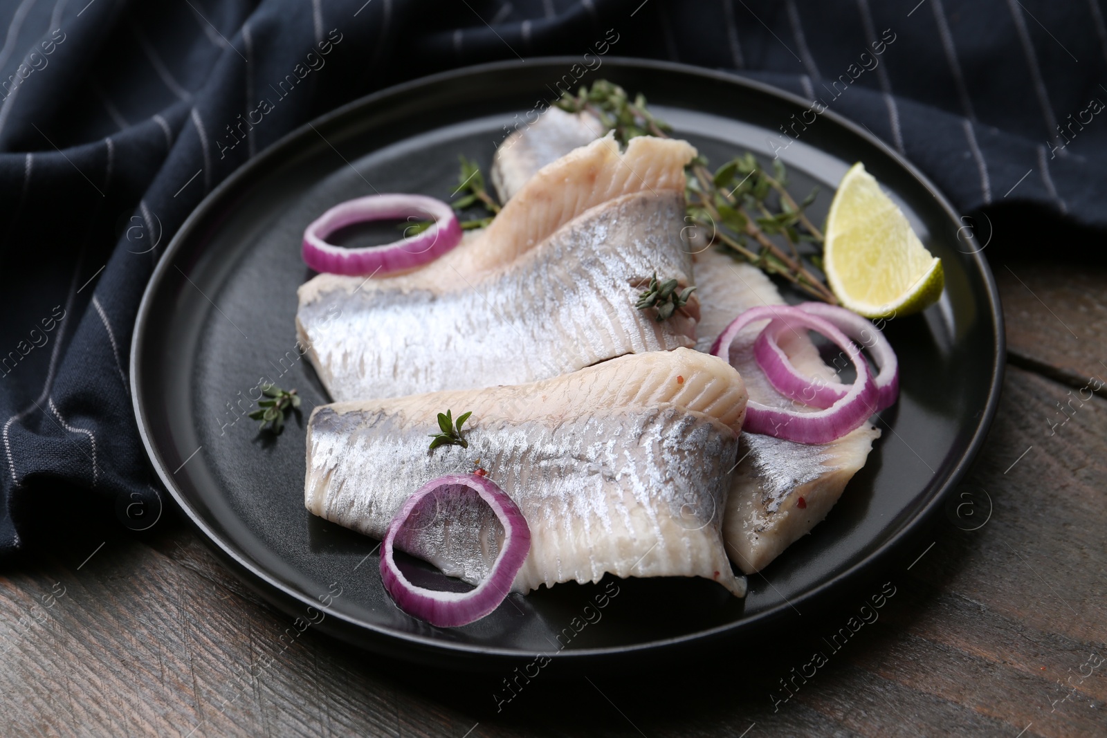 Photo of Marinated herring fillets with onion rings, thyme and lime on wooden table, closeup