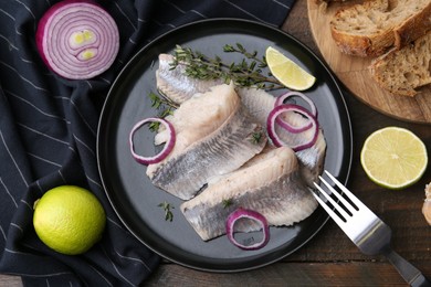 Photo of Marinated herring fillets with onion rings, thyme and lime on wooden table, flat lay