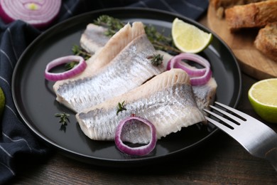 Marinated herring fillets with onion rings, thyme and lime on wooden table, closeup