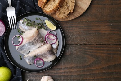 Photo of Marinated herring fillets with onion rings, thyme and lime on wooden table, flat lay. Space for text