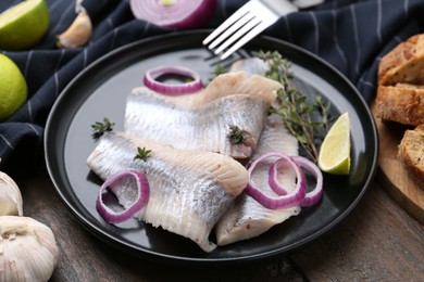 Photo of Marinated herring fillets with onion rings, thyme and lime on wooden table, closeup