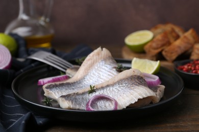 Marinated herring fillets with onion rings, thyme and lime on wooden table, closeup