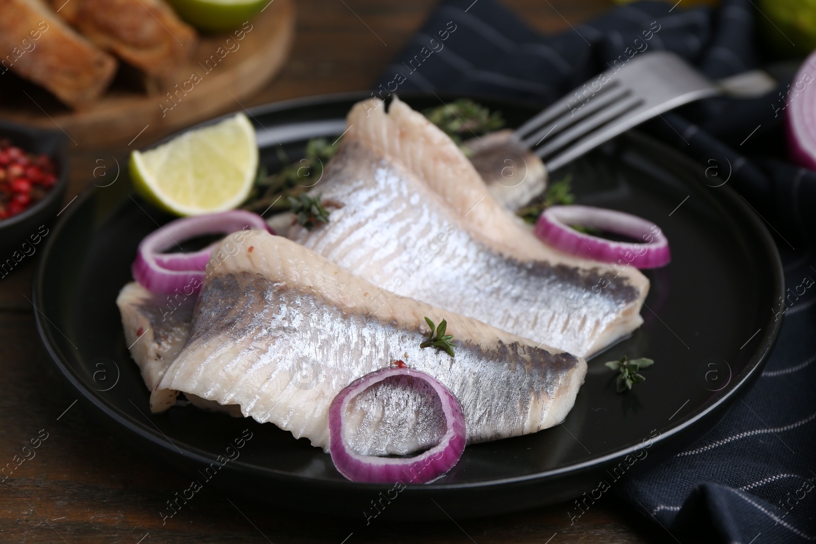 Photo of Marinated herring fillets with onion rings, thyme and lime on wooden table, closeup