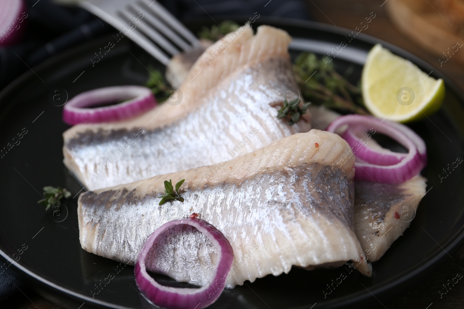 Photo of Marinated herring fillets with onion rings, thyme and lime on table, closeup