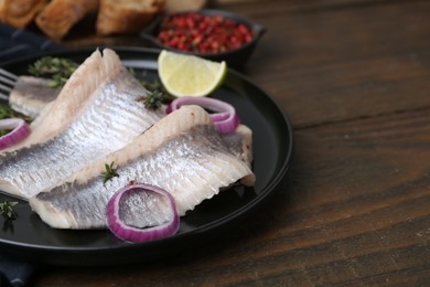 Marinated herring fillets with onion rings, thyme and lime on wooden table, closeup. Space for text