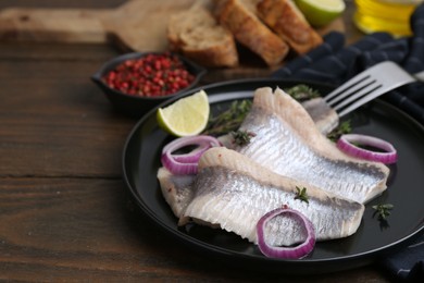 Photo of Marinated herring fillets with onion rings, thyme and lime on wooden table, closeup. Space for text