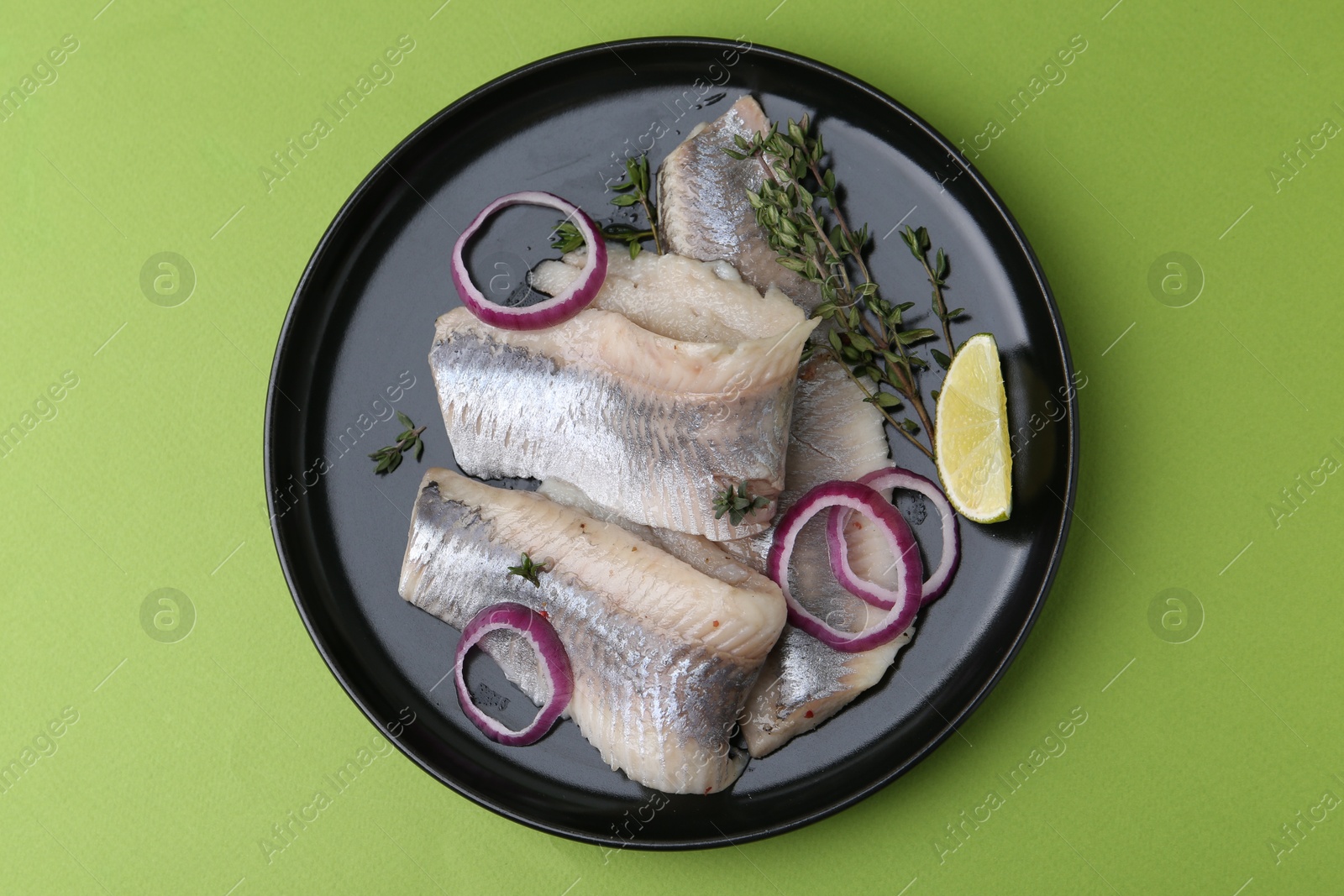 Photo of Marinated herring fillets with onion rings, thyme and lime on green background, top view