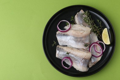 Marinated herring fillets with onion rings, thyme and lime on green background, top view. Space for text