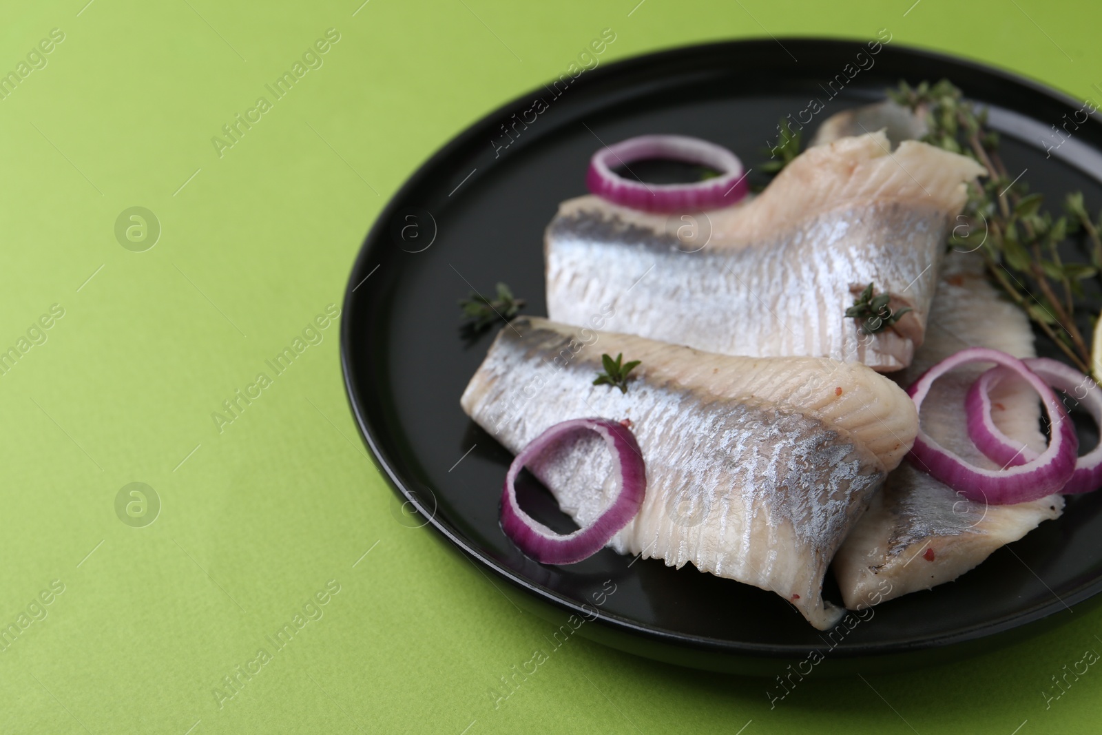 Photo of Marinated herring fillets with onion rings and thyme on green background, closeup. Space for text