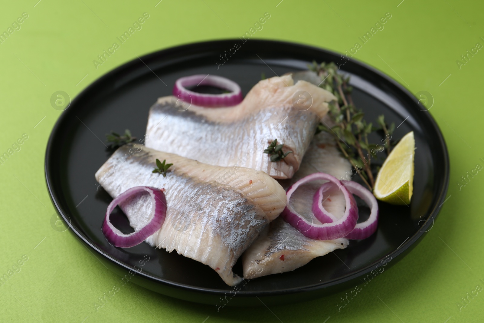 Photo of Marinated herring fillets with onion rings, thyme and lime on green background, closeup